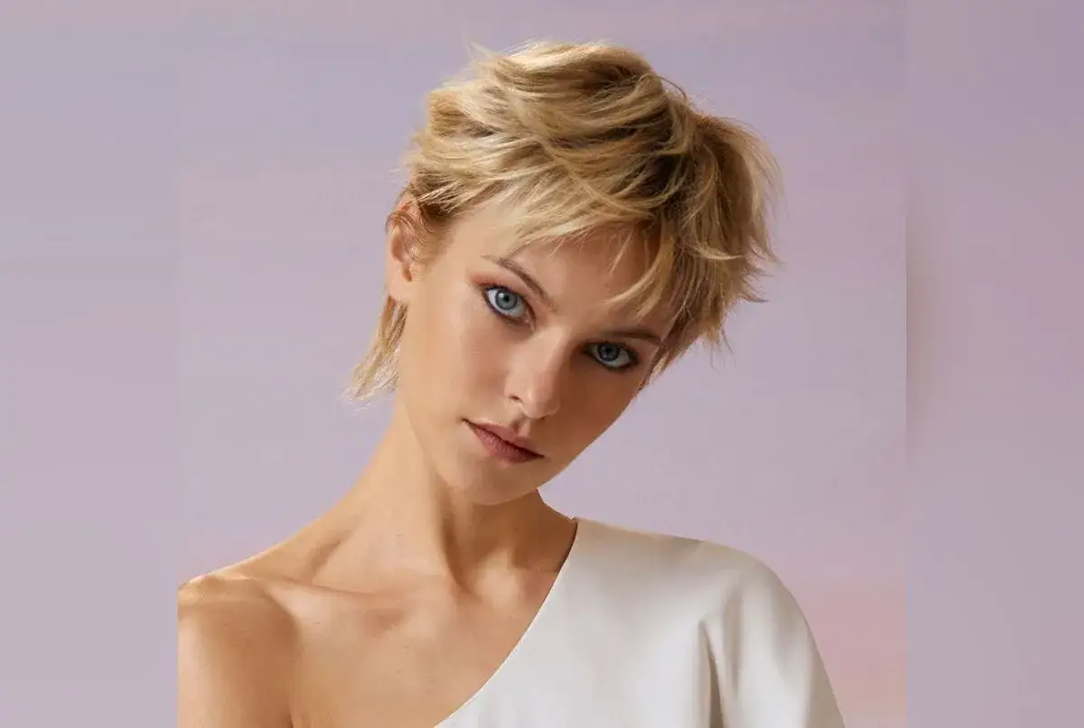 Une femme au regard intense arbore une coupe de cheveux court effilé sauvage, ses mèches blondes dansant avec audace.