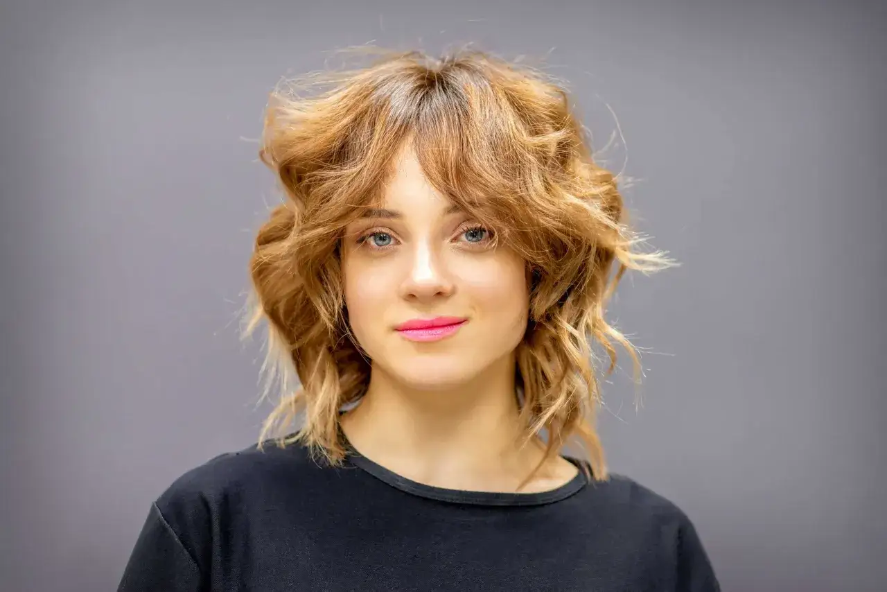 Une femme au regard bleu et aux lèvres roses arbore une coupe wolf cut dégradée et texturisée, un style audacieux et moderne.