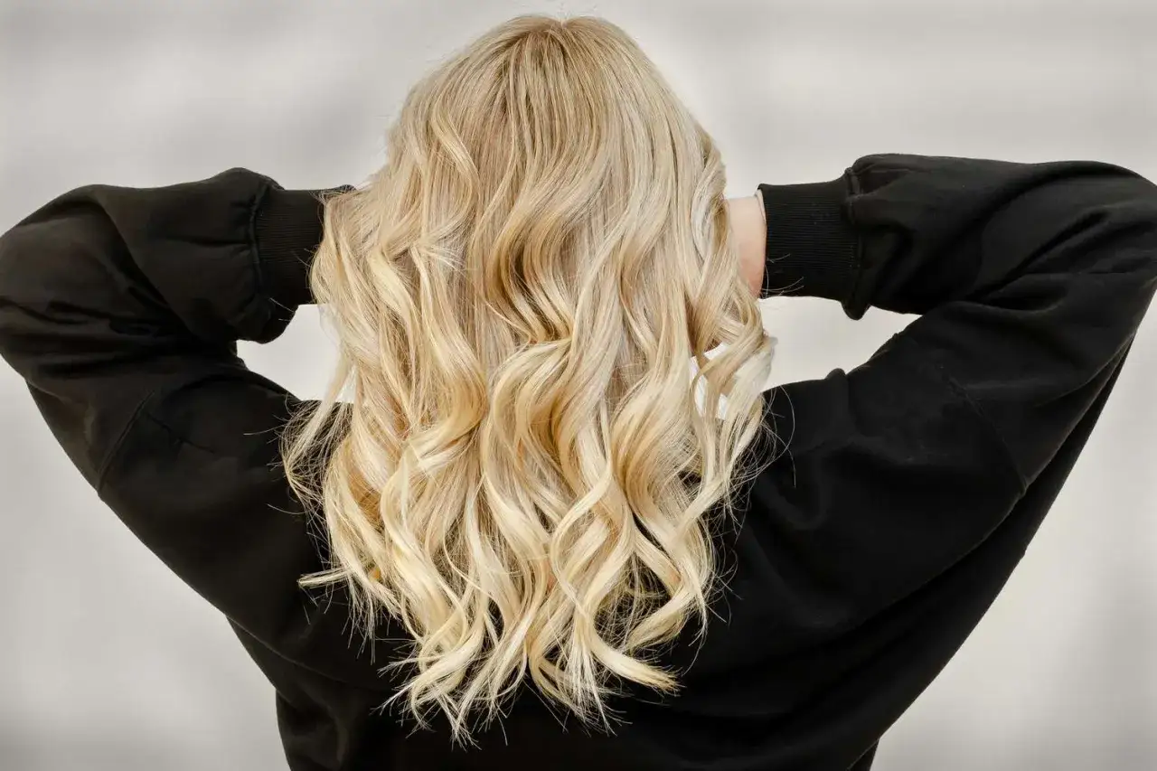 Chevelure blonde ondulée, mains dans les cheveux. Décision : ne plus se lisser les cheveux pendant 1 mois.