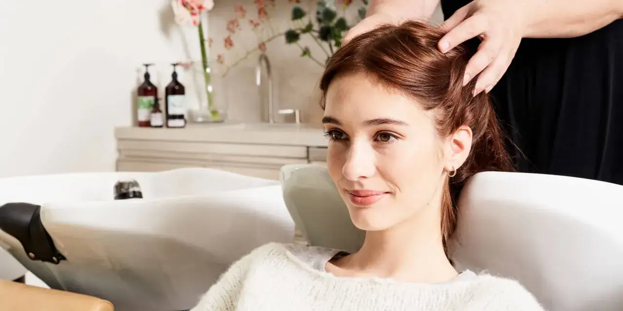 Une femme se fait masser le cuir chevelu dans un salon de coiffure, peut-être pour savoir quand couper ses cheveux pour qu'ils poussent plus vite.