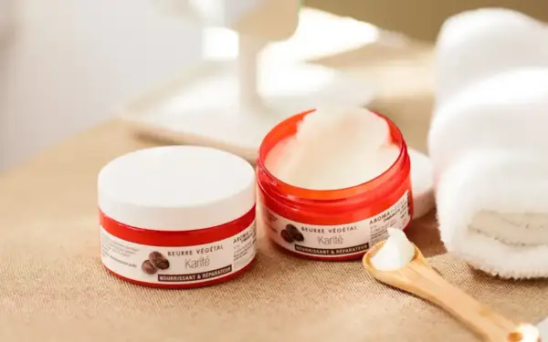 Deux pots de beurre de karité, parfaits pour les bienfaits cheveux. Une cuillère en bois en présente la texture onctueuse.