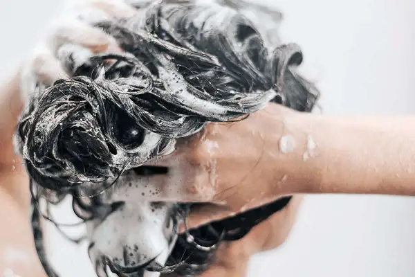 Mousse on dark, wet hair as someone is se laver les cheveux au savon de marseille.