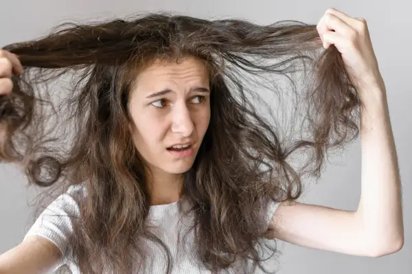 Jeune femme aux cheveux bruns et indisciplinés, se demandant comment faire pour que les cheveux ne gonflent pas. Elle tire sur une mèche, l'air frustrée.