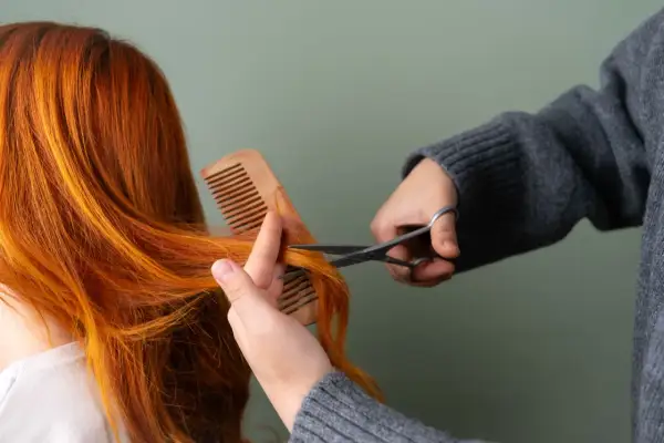 Une personne se coupe les cheveux roux avec des ciseaux, comme si elle se coupait les cheveux avec la lune.