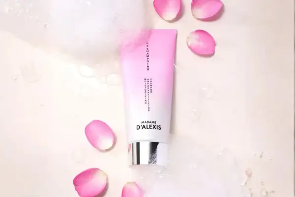 Tube de shampooing rose et blanc, entouré de pétales de rose et de bulles. Idéal pour espacer les shampoings et hydrater vos cheveux.