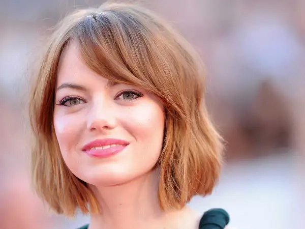Emma Stone, avec sa coupe de cheveux courte et ondulée, met en valeur son visage rond et ses grands yeux verts.