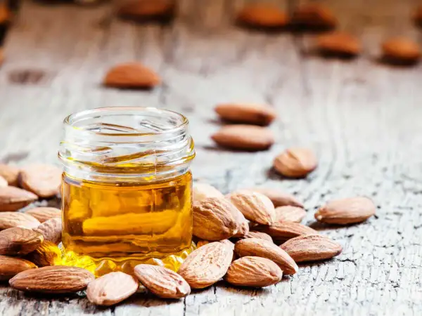 Huile d'amande dorée dans un petit pot, entourée d'amandes. Un secret naturel pour le bienfait des amandes sur les cheveux.