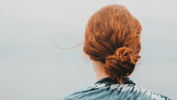 Chevelure rousse coiffée en un chignon facile, quelques mèches s'échappent dans la brise légère.