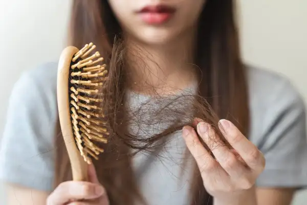 Une femme examine sa brosse à cheveux, remplie de mèches, signe de cheveux cassants.