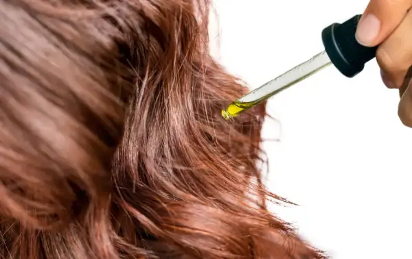 Goutte d'huile de jojoba sur des cheveux bruns, révélant ses bienfaits pour une chevelure éclatante et nourrie.