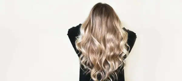 Cheveux châtain transformés en une cascade de mèches blondes lumineuses, un éclaircissement subtil pour un look naturel et ensoleillé.