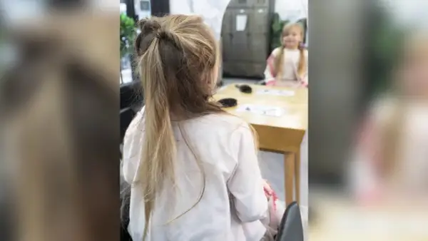 Une petite fille avec une jolie demi queue de cheval torsadée, assise à une table.