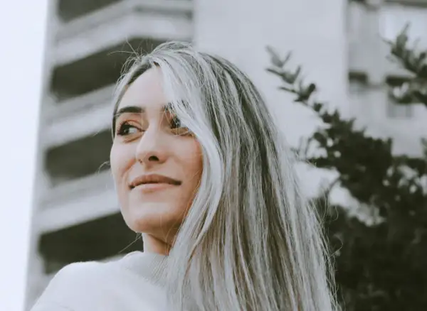 Portrait d'une jeune femme aux cheveux blonds, avec une transition grey blending subtile. Elle regarde au loin, un léger sourire aux lèvres.
