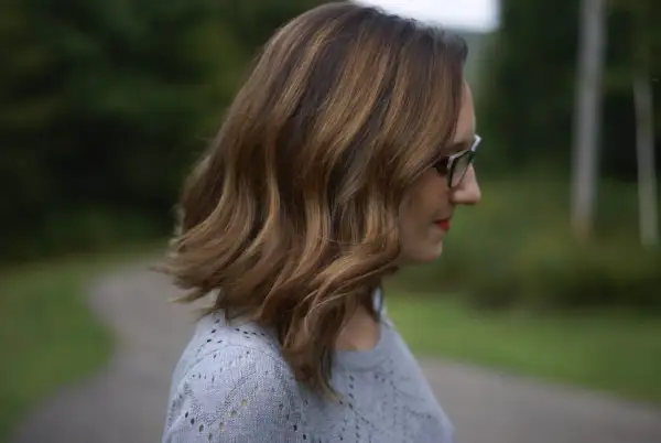Profil d'une femme aux cheveux châtain avec des mèches blanches, portant des lunettes.