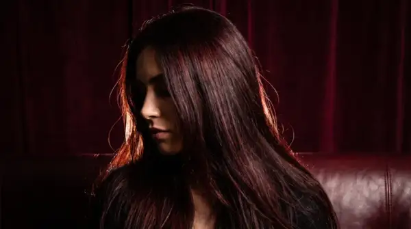 Chevelure brune aux reflets auburn, une femme pose, son visage tourné, comme pour éclaircir cheveux noir sans décoloration.