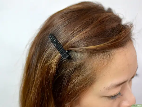 Une mèche de cheveux châtain est fixée avec une barrette noire scintillante. Une coiffure facile pour un look rapide.