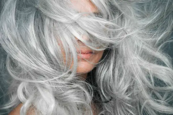 Gros plan sur une femme aux cheveux poivre et sel naturels, une chevelure argentée et volumineuse qui encadre son visage.