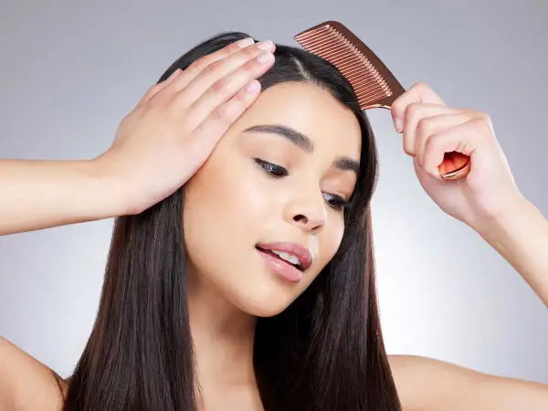 Une femme se peigne les cheveux, montrant comment enlever une raie de cheveux pour un look parfait.