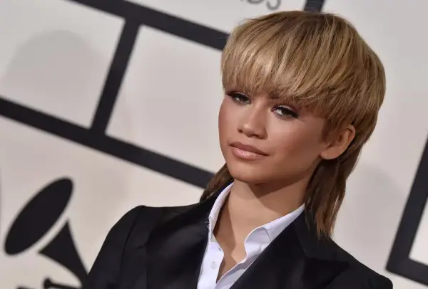 Zendaya arbore une coupe année 80 audacieuse, un mulet blond, avec un blazer noir et une chemise blanche.