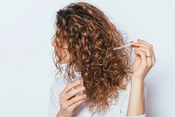 Une femme applique une huile sur ses cheveux bouclés pour définir ses frisottis.